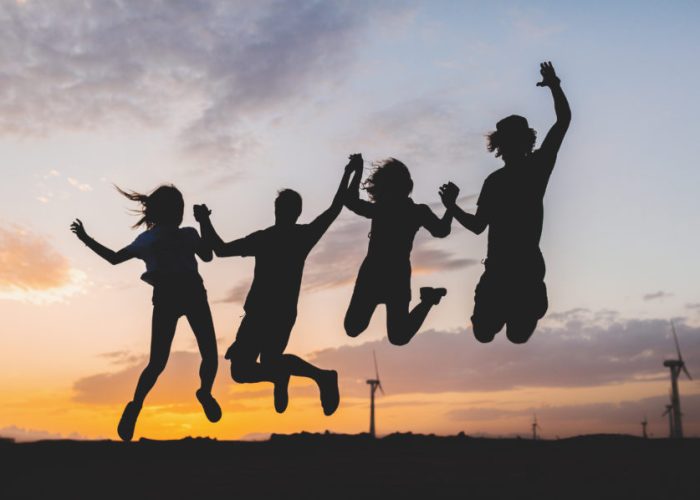 happy hipster friends company silhouettes on sunset desert landscape jumping together holding hands having fun on vacation, young people traveling